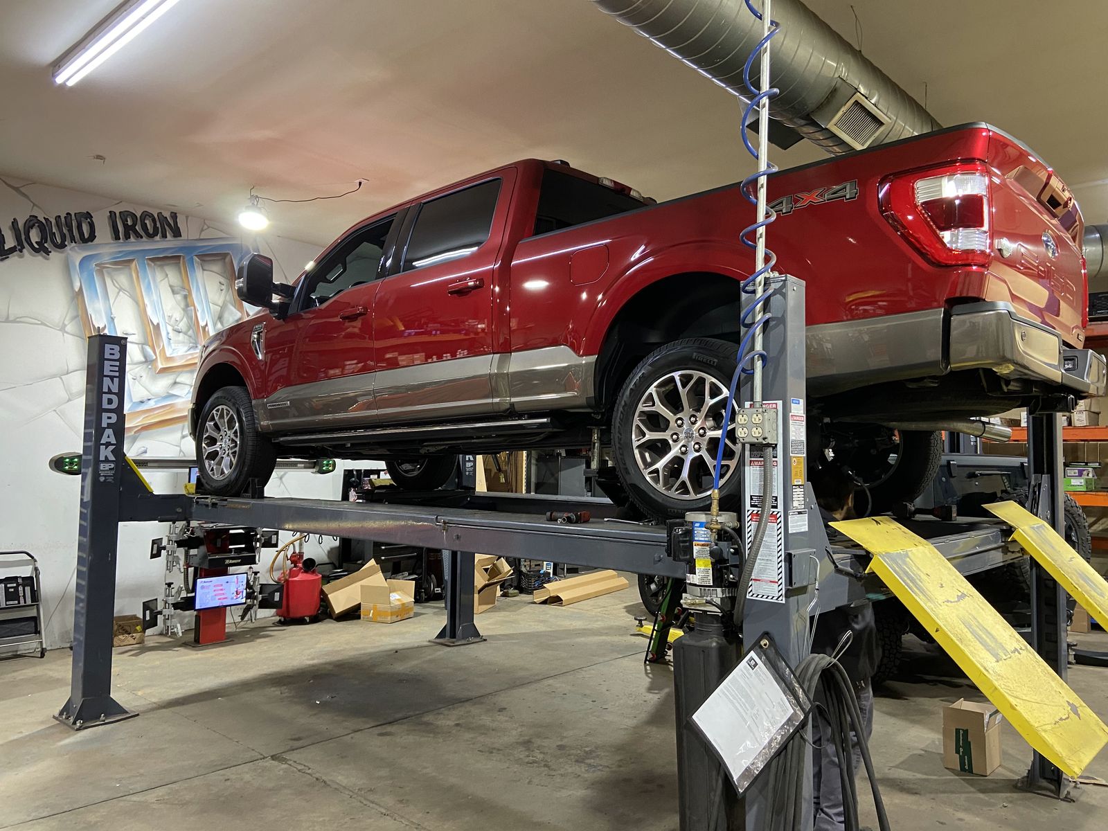 Red Ford F-150 up on a four-post lift in the Liquid Iron service bay